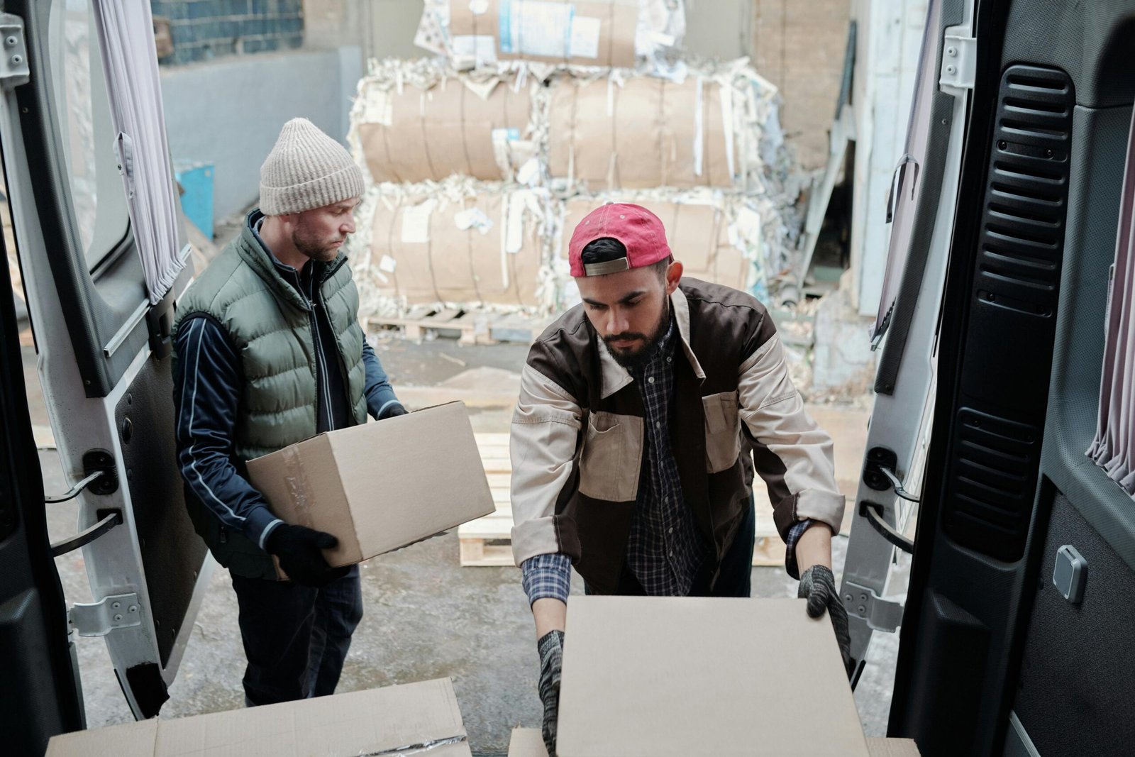 Two delivery workers unloading packages from a van at an industrial site.