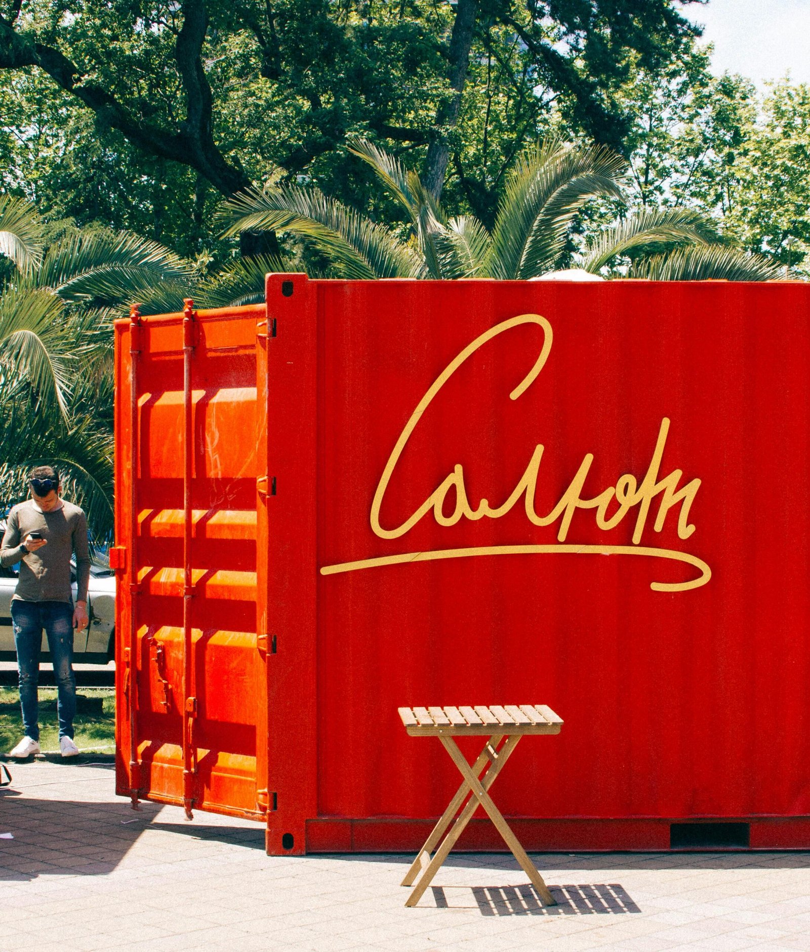 Bright red container with text outdoors amid greenery, sunny day.